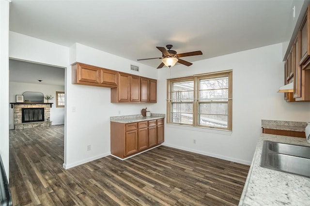 kitchen featuring brown cabinetry, open floor plan, visible vents, and a stone fireplace