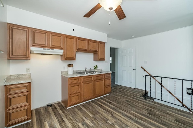 kitchen featuring dark wood-type flooring, brown cabinets, a sink, and under cabinet range hood