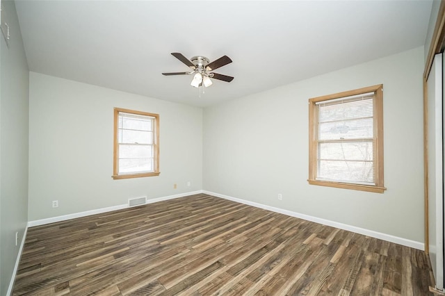 empty room featuring ceiling fan, dark wood-style flooring, visible vents, and baseboards