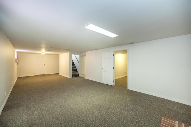 finished below grade area featuring stairs, dark carpet, visible vents, and baseboards