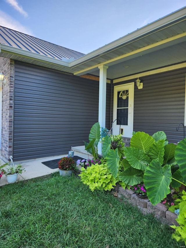 doorway to property with a standing seam roof, brick siding, metal roof, and covered porch