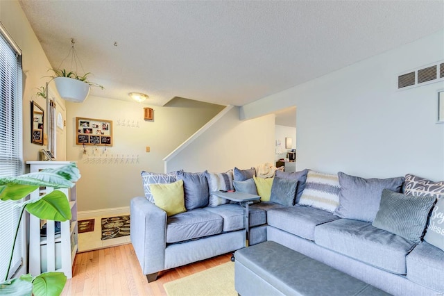 living area with a textured ceiling, light wood-style flooring, stairway, and visible vents