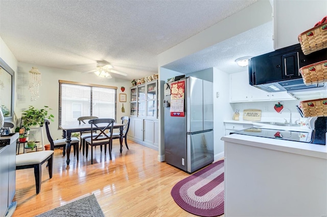 kitchen with freestanding refrigerator, light countertops, a textured ceiling, light wood-type flooring, and a sink