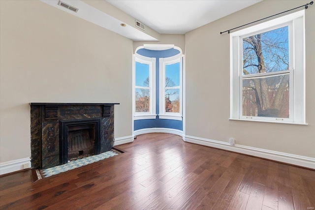 unfurnished living room featuring a fireplace with flush hearth, plenty of natural light, wood finished floors, and visible vents