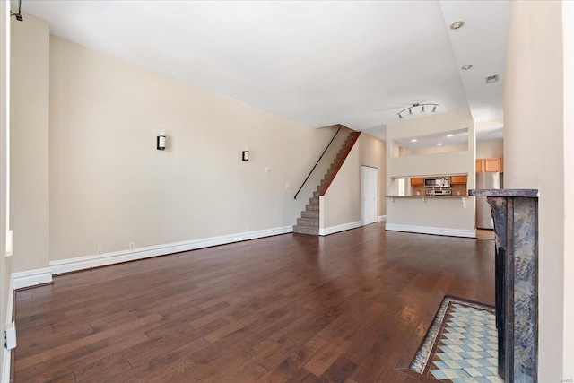 unfurnished living room featuring baseboards, visible vents, stairway, dark wood-style flooring, and track lighting