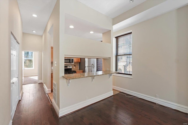 kitchen with a breakfast bar area, wood finished floors, a peninsula, light stone countertops, and stainless steel appliances