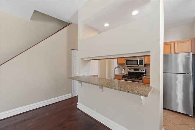 kitchen with baseboards, light stone counters, a peninsula, stainless steel appliances, and a kitchen bar