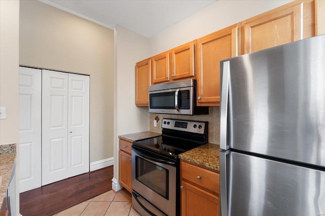 kitchen with light tile patterned floors, stainless steel appliances, baseboards, backsplash, and dark stone countertops