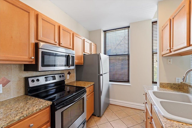 kitchen with light tile patterned floors, backsplash, light stone countertops, stainless steel appliances, and a sink