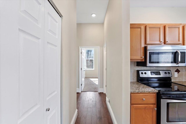 kitchen with stainless steel appliances, dark wood-type flooring, baseboards, backsplash, and dark stone countertops