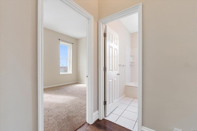 hall featuring baseboards and light colored carpet