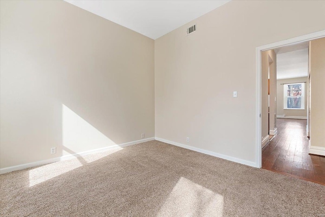 unfurnished room featuring baseboards, visible vents, dark colored carpet, and dark wood finished floors