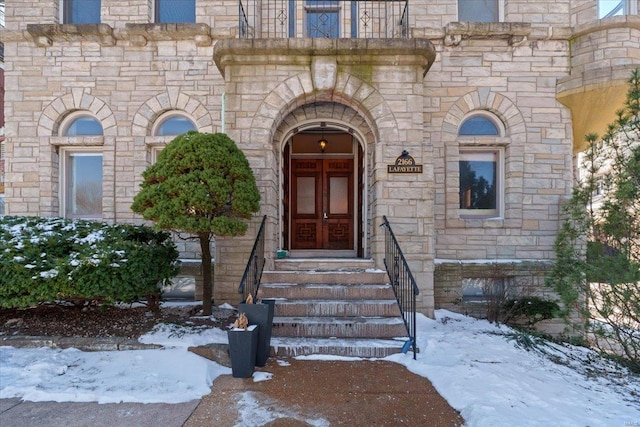 snow covered property entrance with stone siding