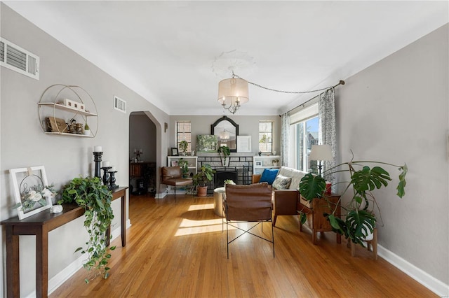 living area featuring a stone fireplace, arched walkways, visible vents, and light wood-type flooring