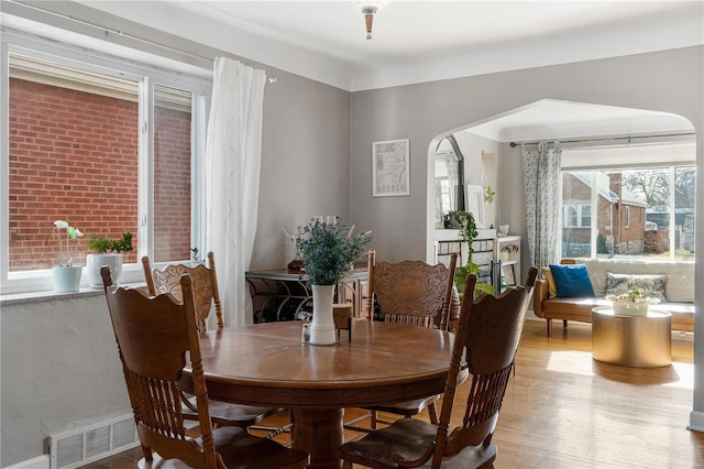 dining area with light wood-style floors, arched walkways, and visible vents