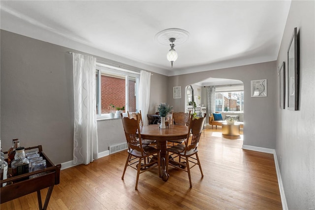 dining area featuring wood finished floors, visible vents, arched walkways, and baseboards