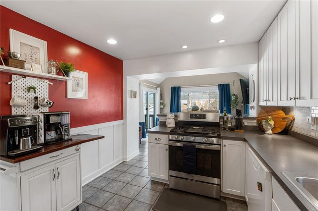 kitchen featuring stainless steel gas range oven, a wainscoted wall, dark countertops, white cabinets, and white dishwasher