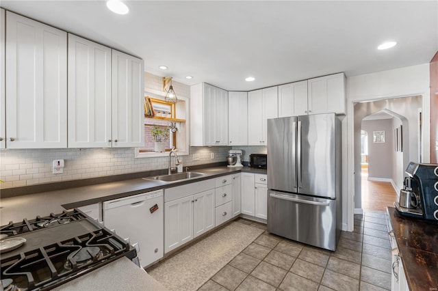 kitchen featuring a sink, dark countertops, freestanding refrigerator, arched walkways, and white dishwasher