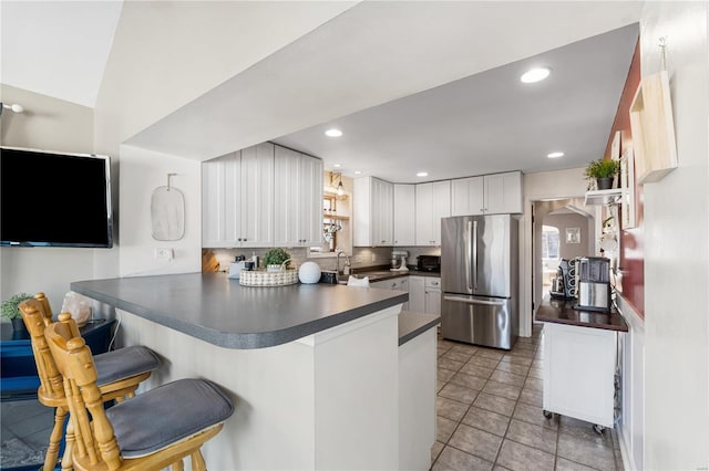 kitchen featuring arched walkways, dark countertops, a peninsula, and freestanding refrigerator