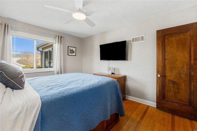 bedroom featuring ceiling fan, visible vents, baseboards, and wood finished floors