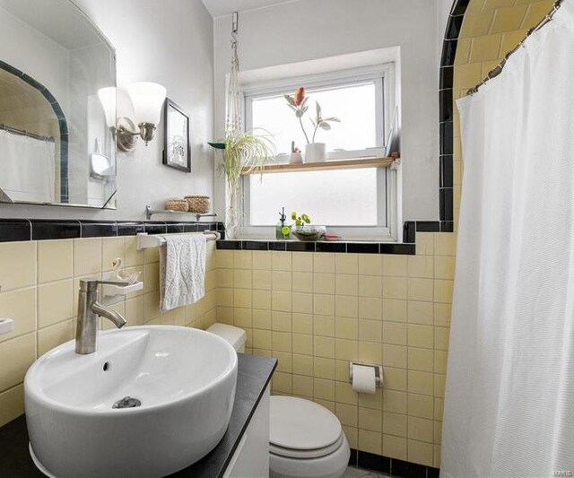 bathroom featuring curtained shower, tile walls, toilet, and a sink