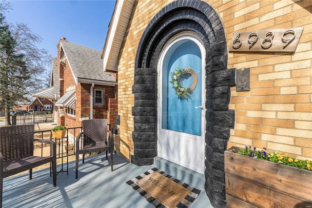 view of exterior entry with brick siding and a shingled roof