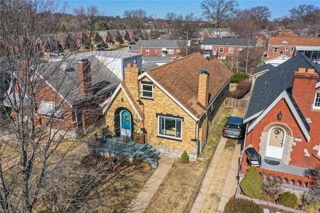 view of front facade featuring dirt driveway, a residential view, roof with shingles, brick siding, and a chimney