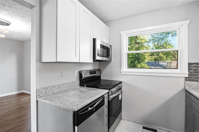 kitchen with light hardwood / wood-style flooring, stainless steel appliances, light stone counters, a textured ceiling, and white cabinets
