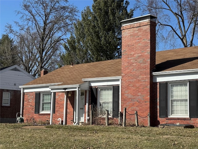 view of front of home featuring a shingled roof, a chimney, a front lawn, and brick siding