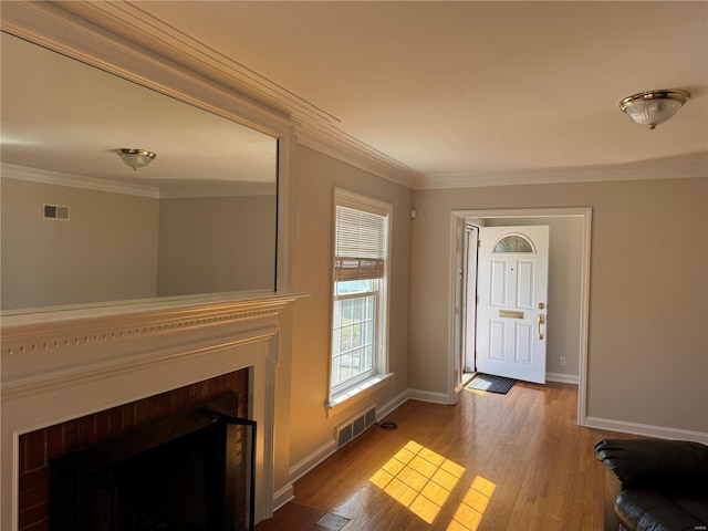 foyer featuring a fireplace with flush hearth, visible vents, ornamental molding, and wood finished floors