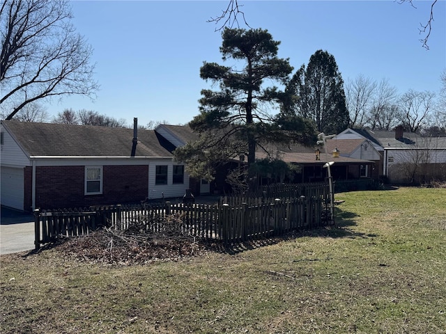 rear view of property with an attached garage, a yard, a fenced front yard, and brick siding