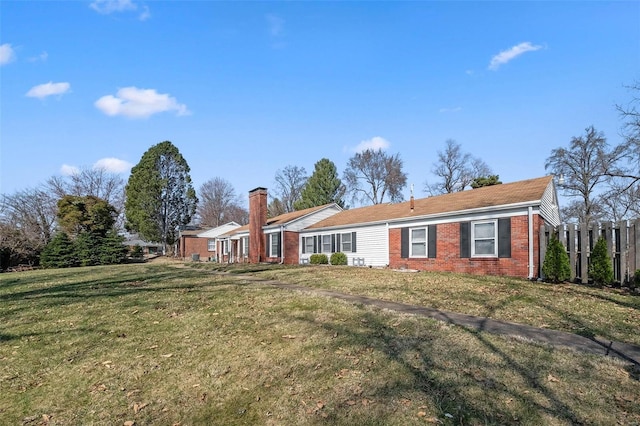 view of front facade featuring brick siding, a chimney, a front lawn, and fence