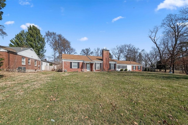 back of house with brick siding, a chimney, and a yard