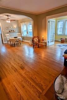 living area with arched walkways, ceiling fan, ornamental molding, and wood finished floors