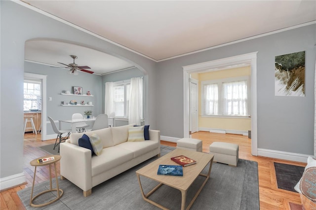 living room with arched walkways, ornamental molding, wood finished floors, and a healthy amount of sunlight