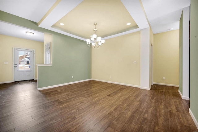 empty room featuring dark wood-type flooring, a chandelier, and a raised ceiling