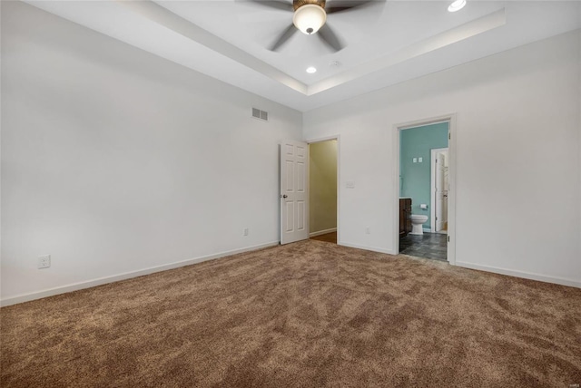 unfurnished bedroom with connected bathroom, ceiling fan, a tray ceiling, and carpet flooring