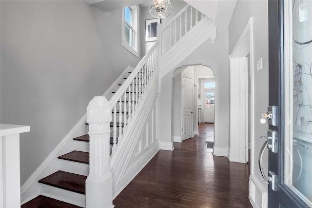 foyer with arched walkways, dark wood finished floors, a towering ceiling, baseboards, and stairs