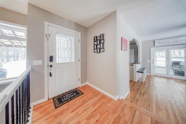 entryway featuring arched walkways, light wood-style floors, and baseboards