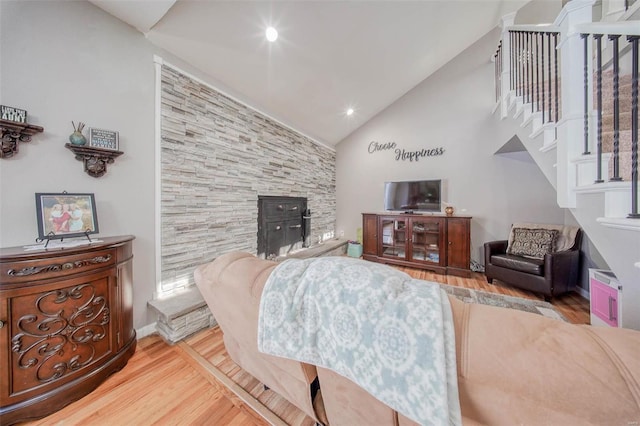 living area featuring stairway, wood finished floors, high vaulted ceiling, and a wood stove