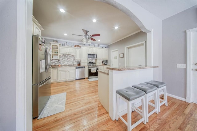 kitchen featuring stainless steel appliances, arched walkways, a ceiling fan, light stone countertops, and a kitchen breakfast bar