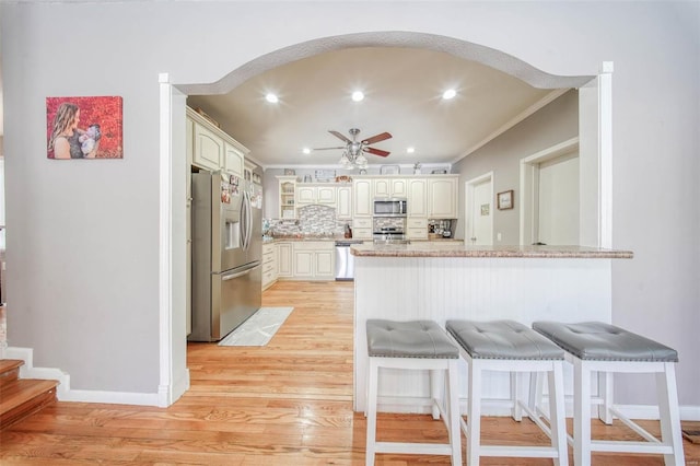 kitchen featuring stainless steel appliances, a peninsula, light wood-style floors, decorative backsplash, and a kitchen bar