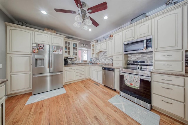 kitchen featuring stainless steel appliances, crown molding, ceiling fan, light wood-type flooring, and glass insert cabinets