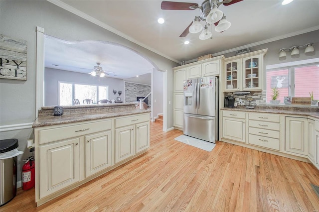 kitchen with stainless steel fridge, ceiling fan, glass insert cabinets, crown molding, and arched walkways