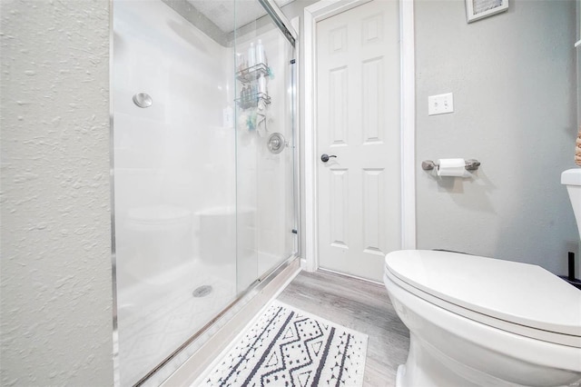 bathroom with toilet, a shower stall, a textured wall, and wood finished floors