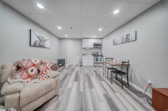 living area featuring light wood-style floors, baseboards, recessed lighting, a paneled ceiling, and a textured wall