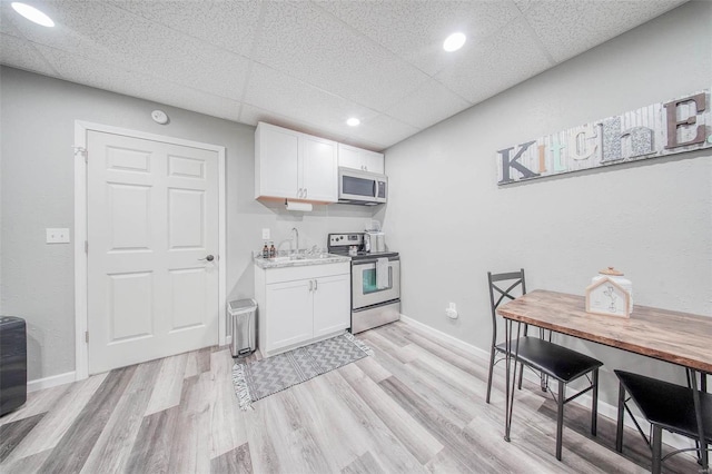 kitchen with stainless steel appliances, white cabinets, a sink, light wood-style floors, and a paneled ceiling