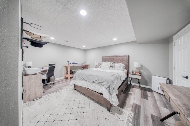 bedroom featuring wood finished floors, a desk, recessed lighting, a paneled ceiling, and baseboards