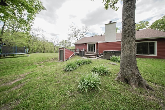 rear view of house featuring a hot tub, a trampoline, a chimney, a lawn, and central AC