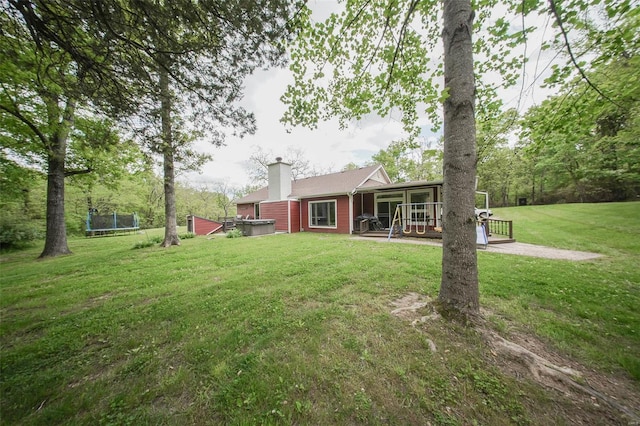 view of grassy yard featuring a trampoline, a sunroom, and a hot tub